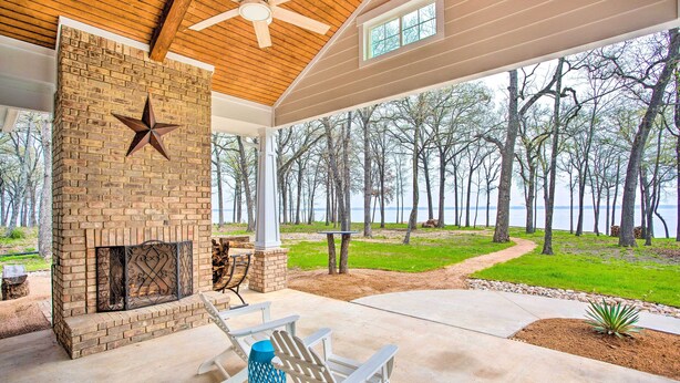 A covered patio with a brick fireplace, Adirondack chairs, and a view of trees and water. - Waterfront Lake Tawakoni Home w/ Fire Pit! (Quinlan)