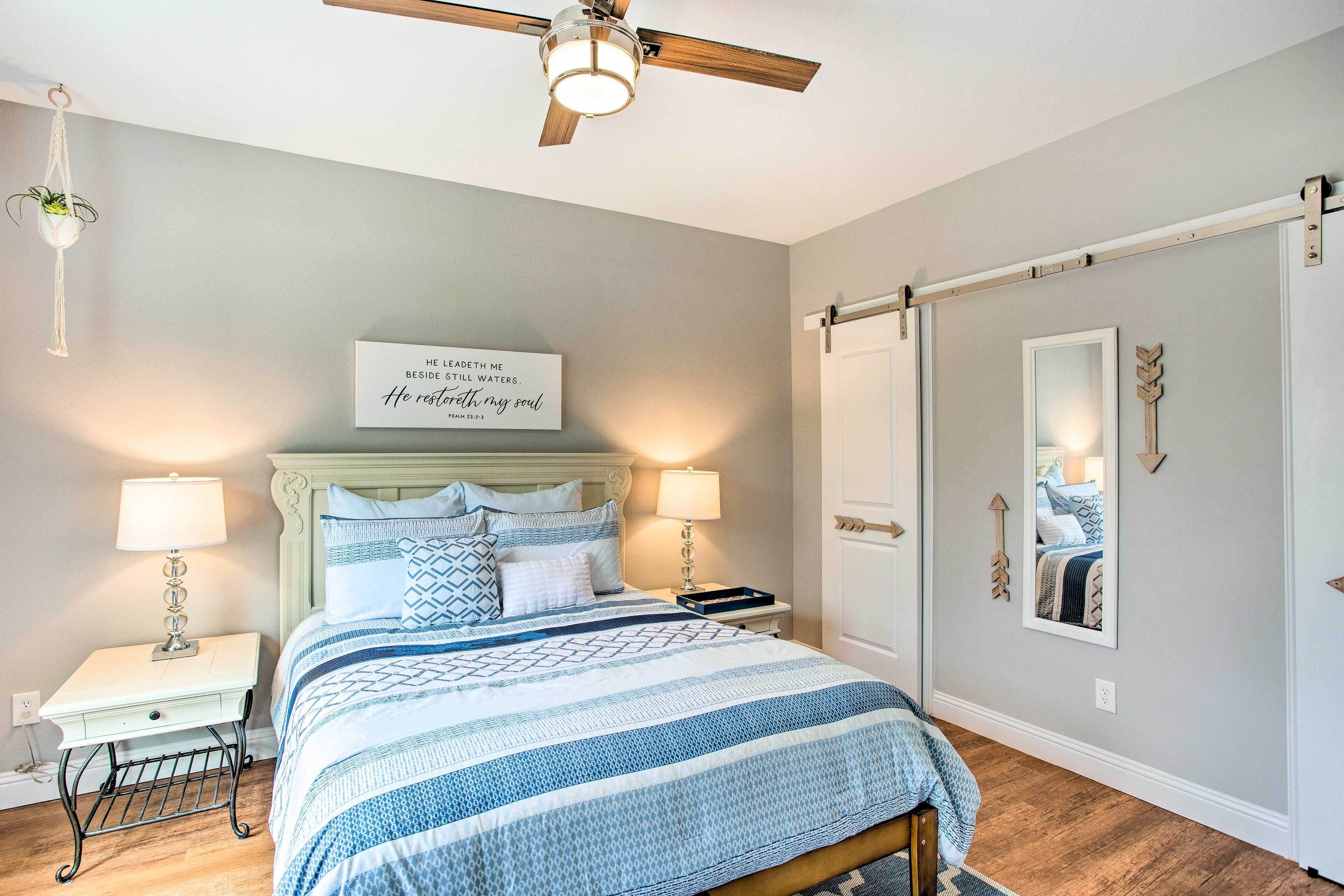 A bedroom with a bed, bedside lamps, a ceiling fan, a wall-mounted mirror, and a motivational quote.