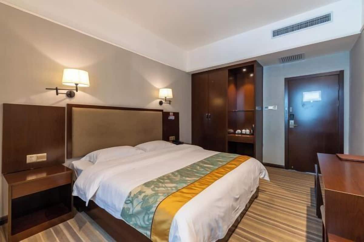 A hotel room with a large bed, a wooden headboard, a nightstand, a desk, and a wardrobe.