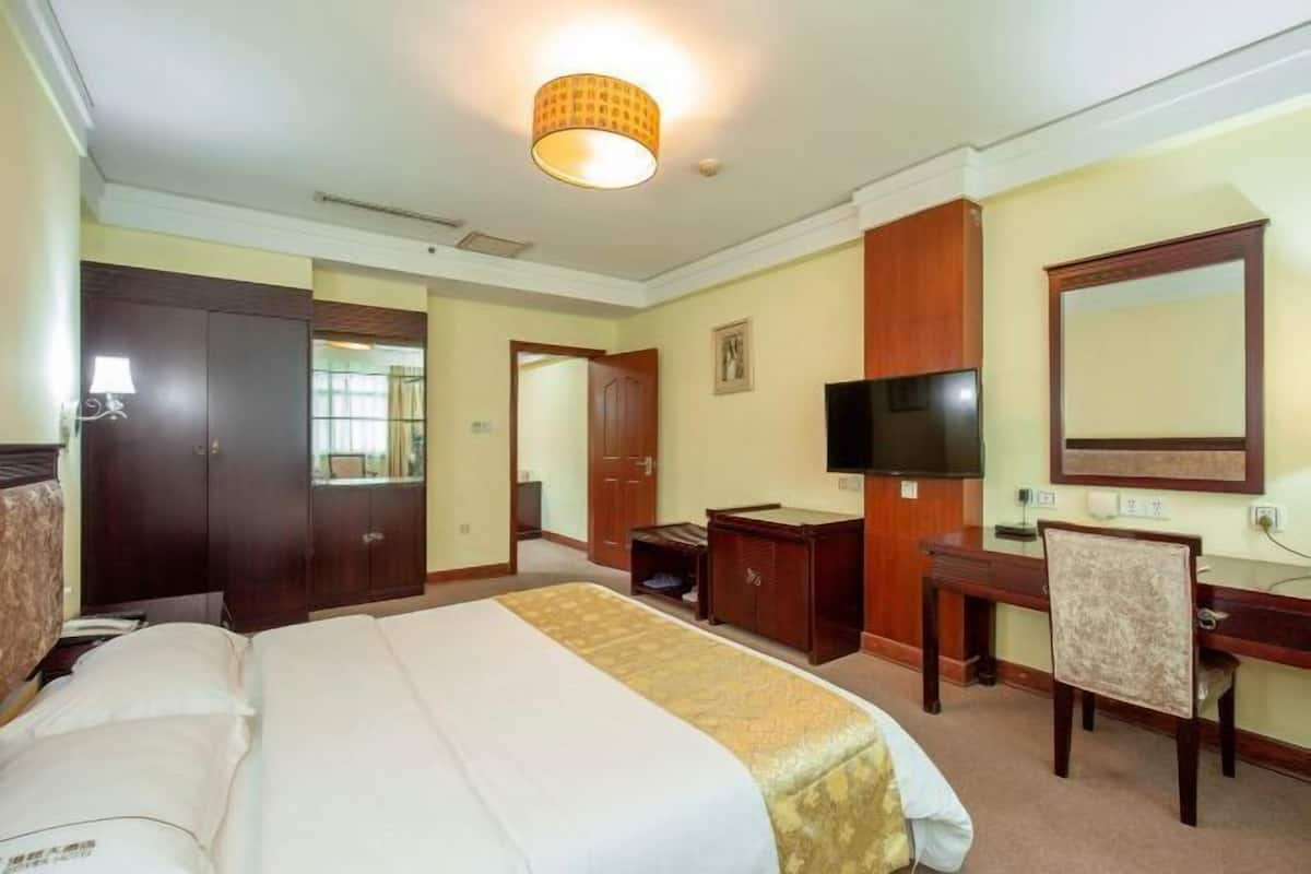 A hotel room with a large bed, a desk, a chair, a television, and a wardrobe.