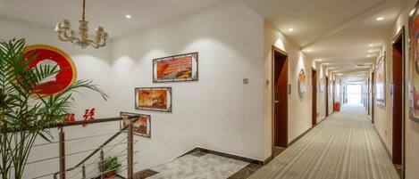 Un pasillo de hotel con piso alfombrado, una escalera con barandilla y cuadros en las paredes.