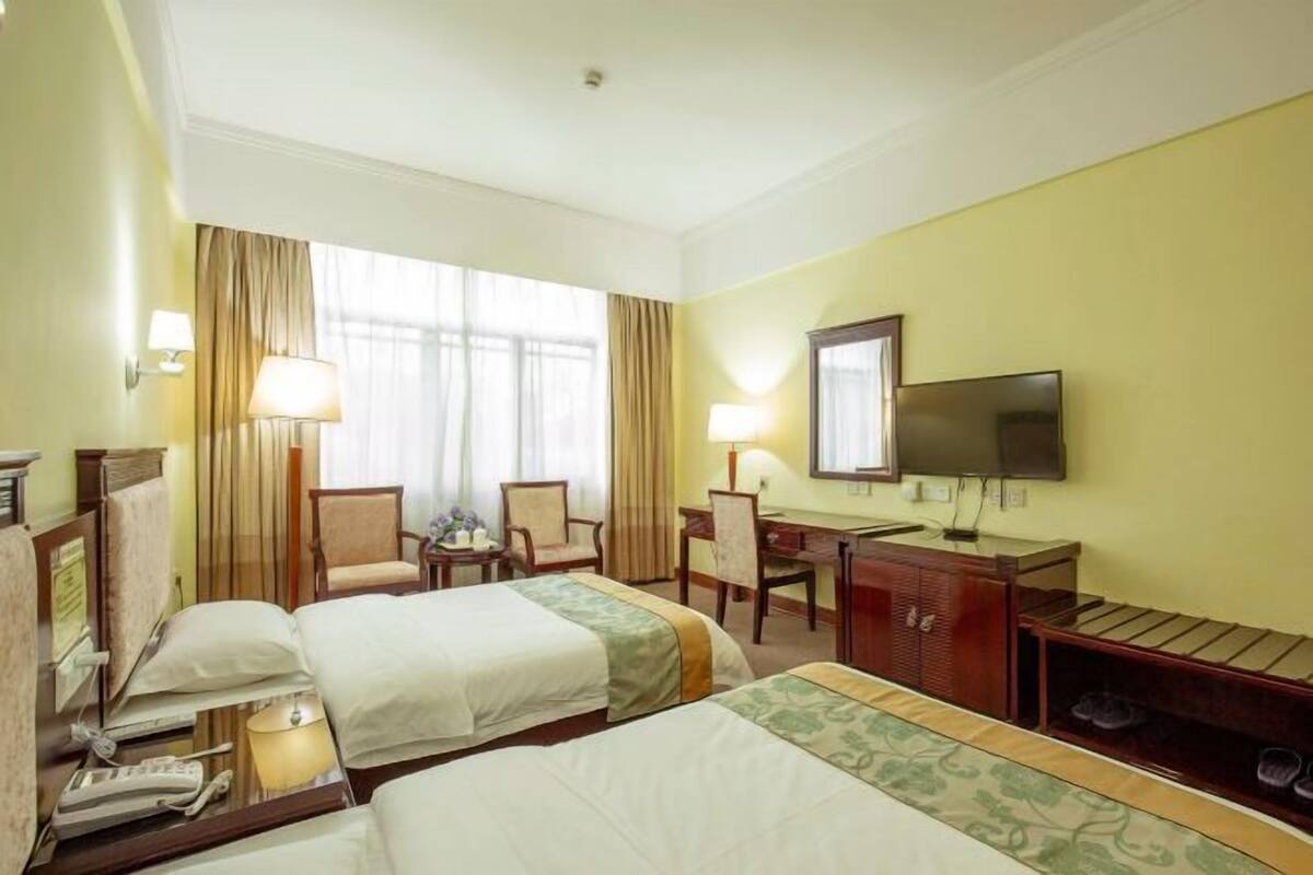 A hotel room with two beds, a desk, a chair, a TV, and a shoe rack.