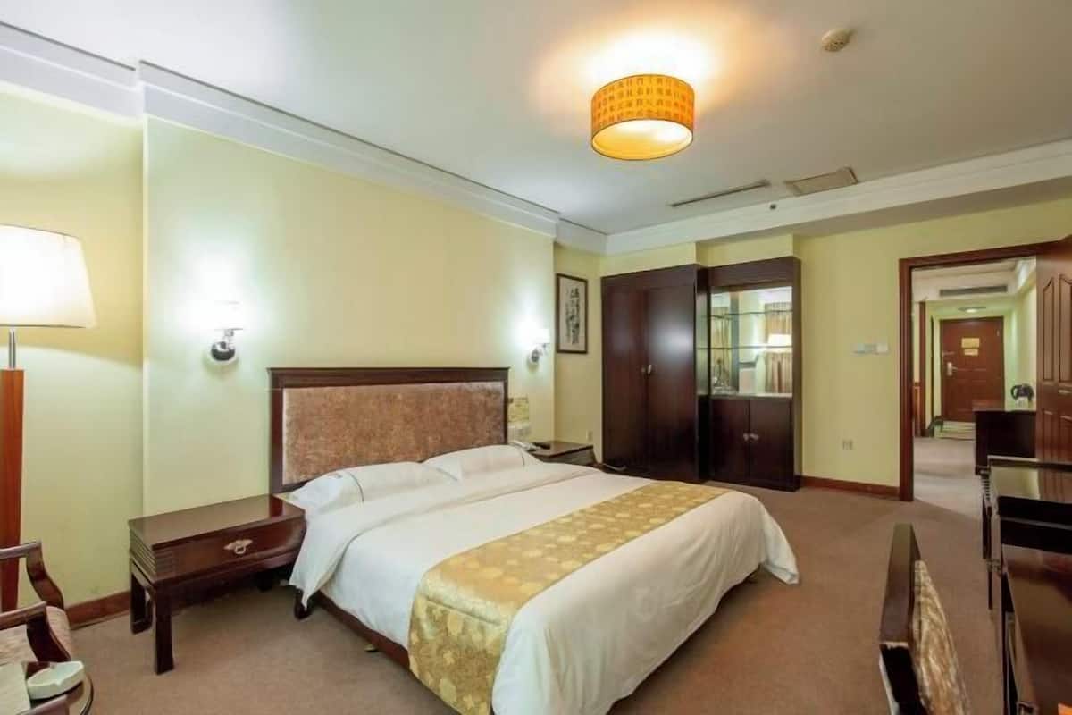 A hotel room with a large bed, bedside tables, a wardrobe, and a desk with a chair.