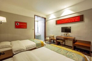 Habitación de hotel con dos camas, un escritorio, una silla, un televisor y un zapatero.