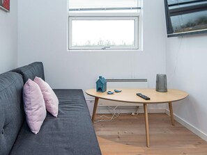 Une pièce moderne avec un canapé gris, une petite table ronde, une maquette de maison bleue et un téléviseur fixé au mur.