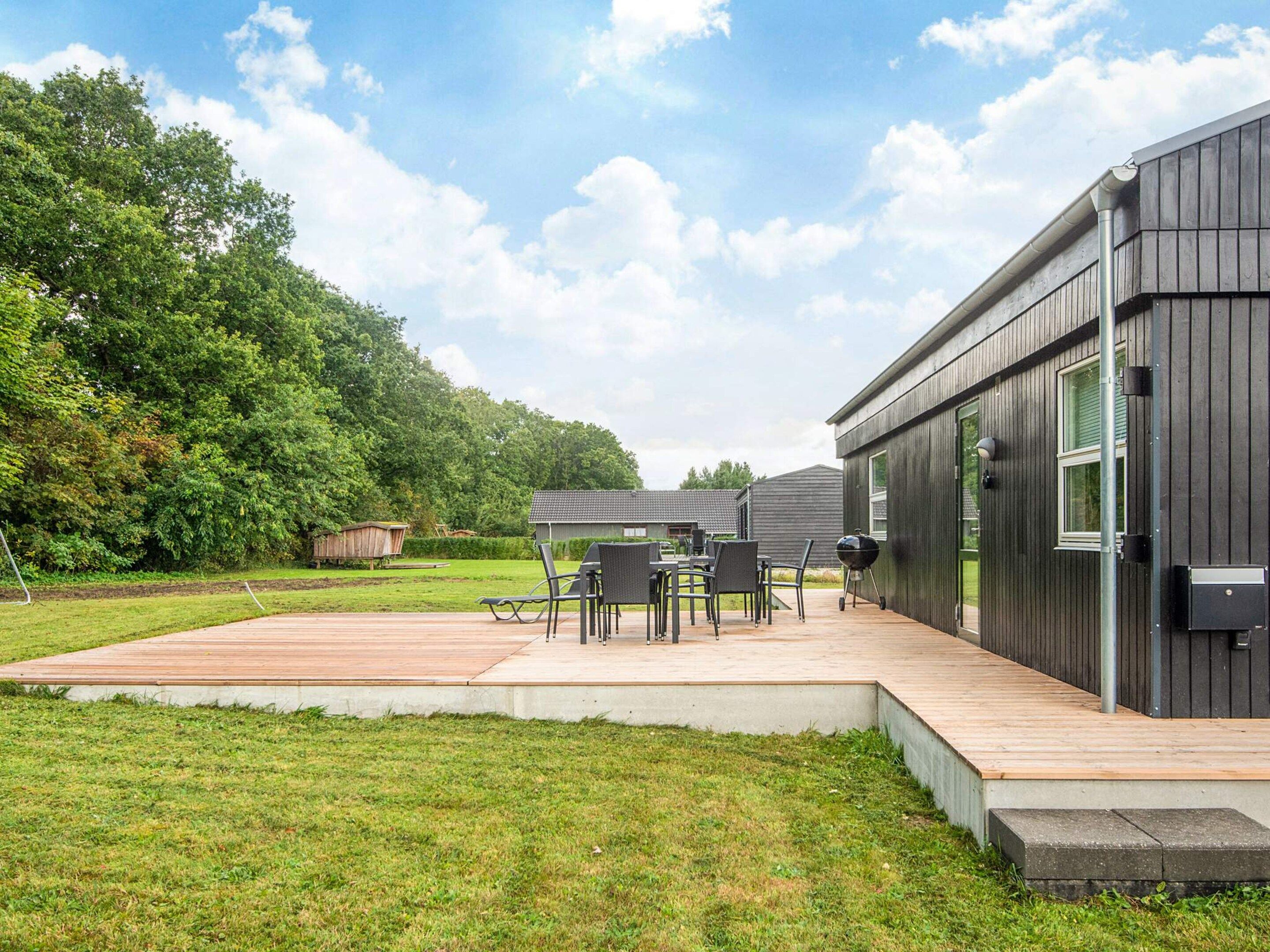 A modern outdoor patio with a wooden deck, a dining table with chairs, and a barbecue grill.