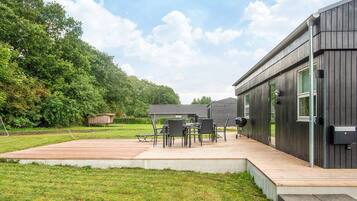 A modern outdoor patio with a wooden deck, a dining table with chairs, and a barbecue grill.