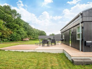 A modern outdoor patio with a wooden deck, a dining table with chairs, and a barbecue grill. - 5 Person Holiday Home in Ansager (Ansager)