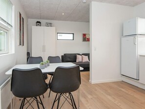 A modern kitchen with a white refrigerator, a dining table with four chairs, and a grey sofa in the background. - 5 Person Holiday Home in Ansager (Ansager)