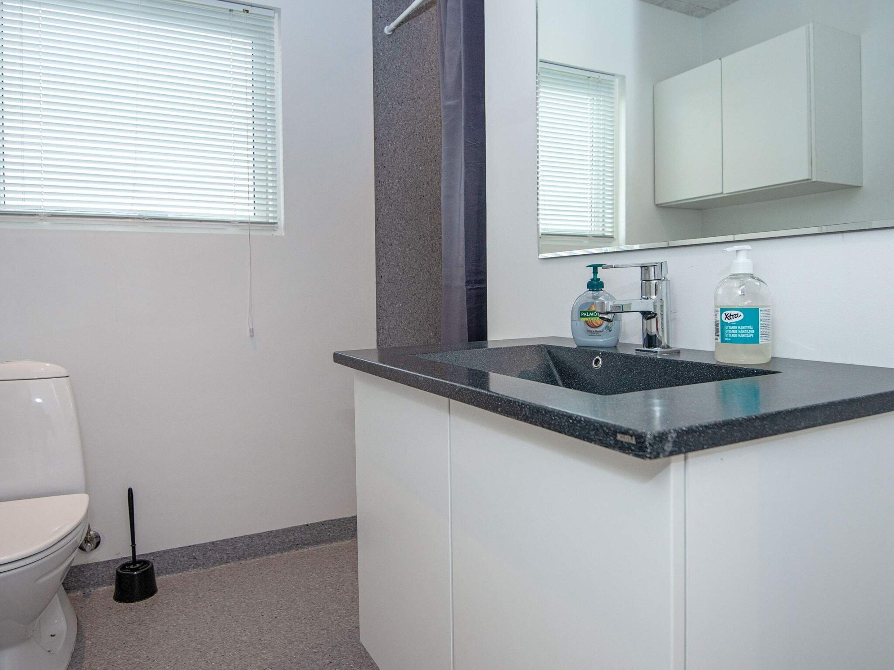 A bathroom with a toilet, sink, mirror, and a bottle of hand sanitizer.