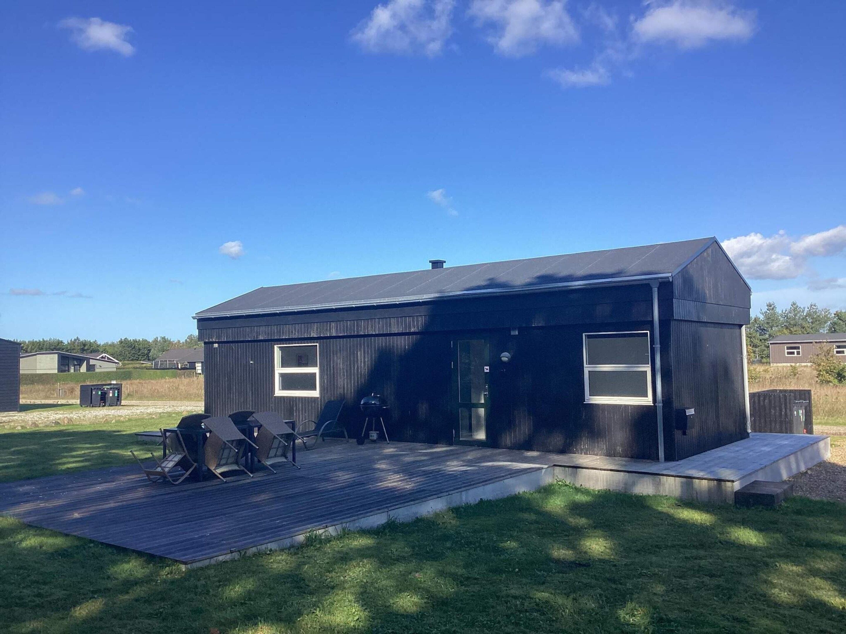 A modern black building with a flat roof, a covered patio area with seating, and a clear sky.