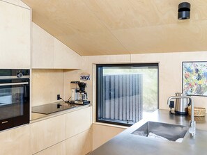 Cozinha moderna com armários de madeira, forno embutido, cafeteira e janela com vista.