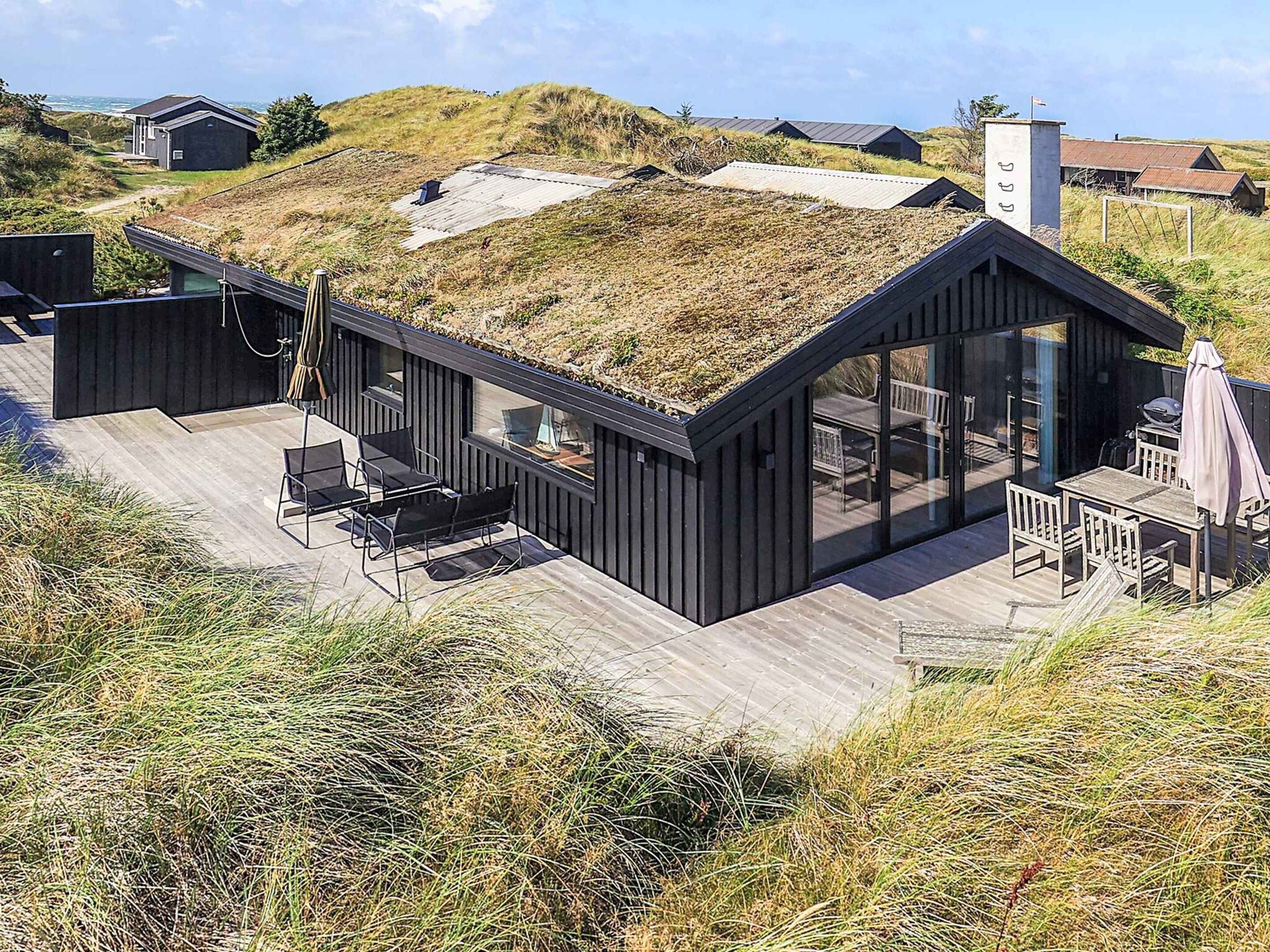 A modern beach house with a flat roof, large glass windows, and a deck with outdoor furniture.