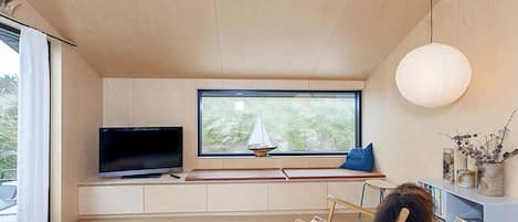 A modern living room with a television, a large window with a sailboat view, a round white rug, and a bookshelf with books and decorative items.