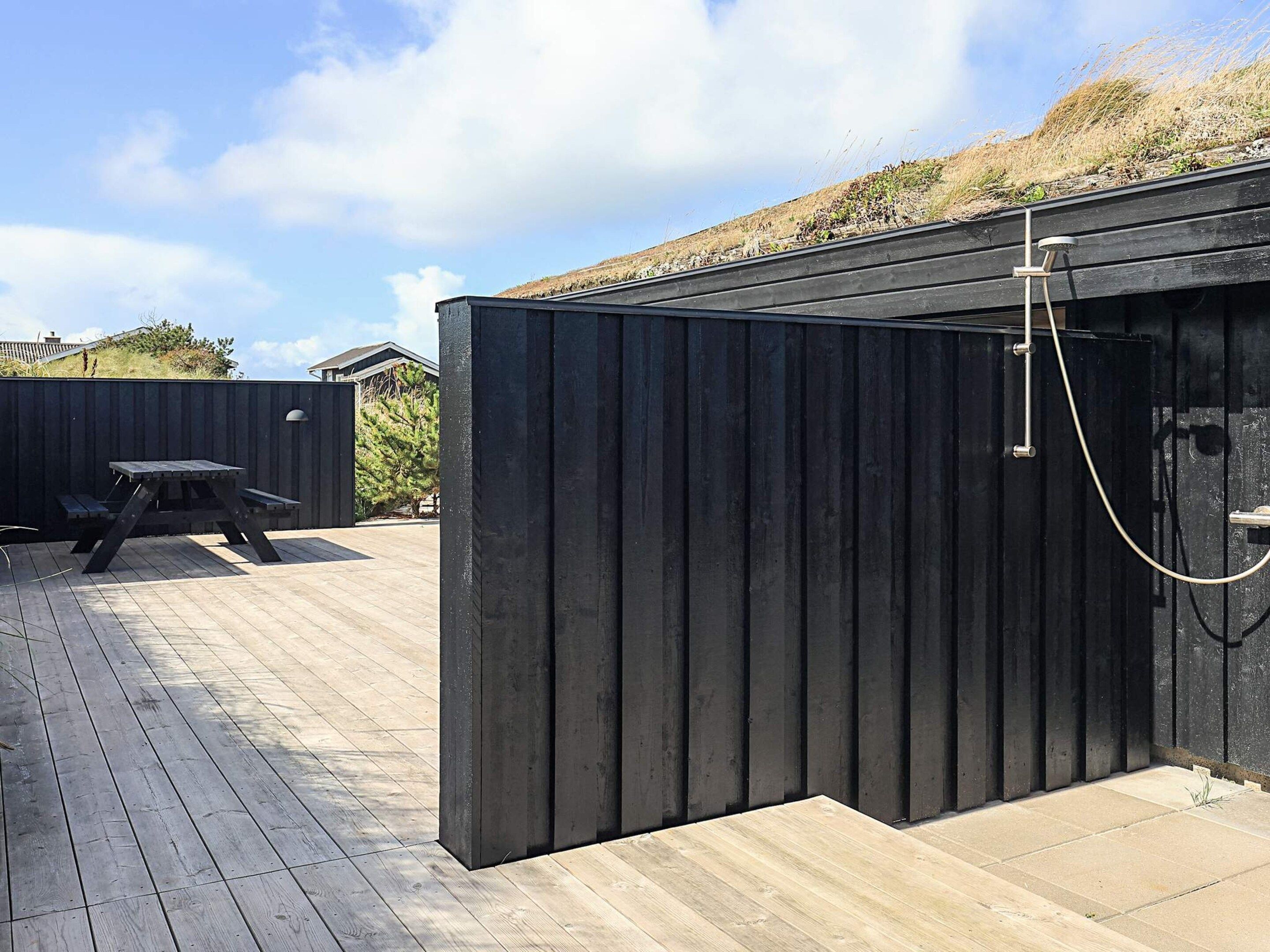 Een houten terras met een picknicktafel en een zwarte metalen constructie, mogelijk een tuinhuis of opslagruimte.