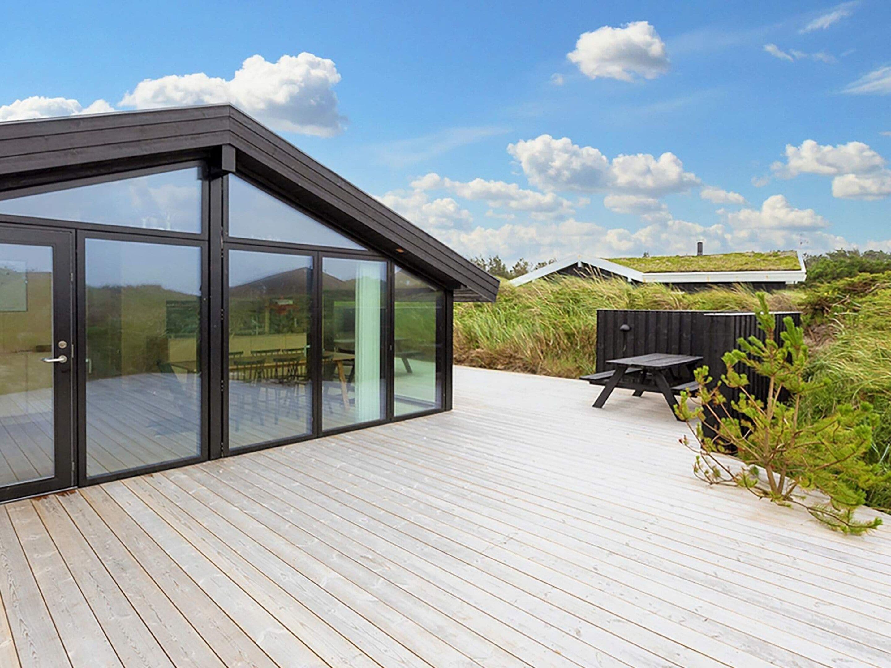 A modern building with large glass doors, a wooden deck, and a view of the surrounding landscape.