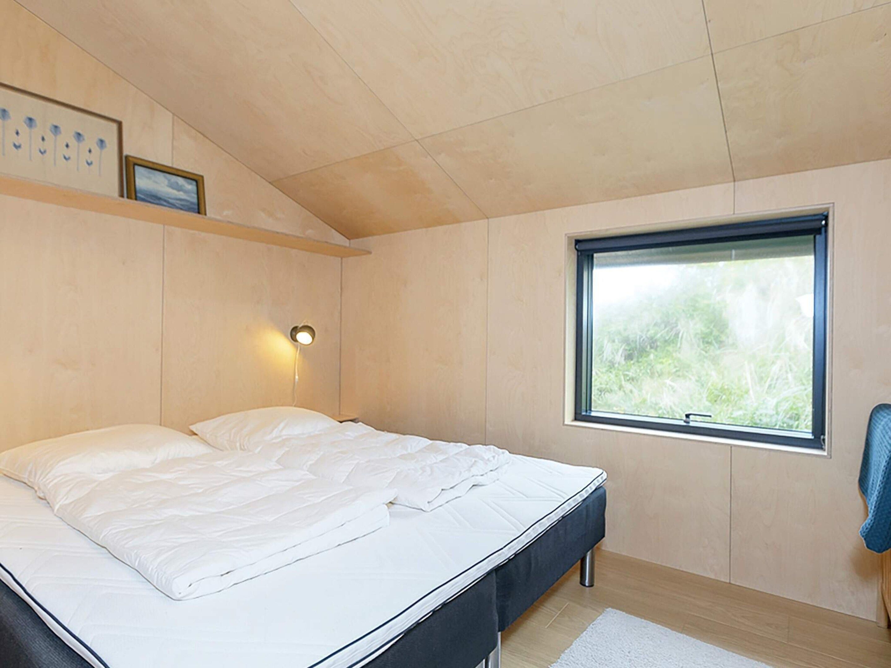 Un dormitorio con una cama, una lámpara de pared, una ventana y una toalla azul en una silla.