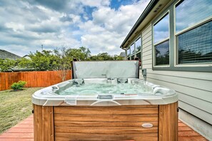 Un jacuzzi en un patio trasero con una terraza de madera, un cerco de madera y una casa al fondo.
