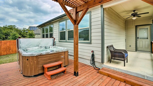 Een houten terras met een jacuzzi, een bank en een overdekte patio met een plafondventilator.