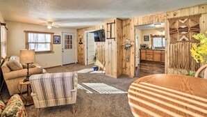 Ein gemütliches Wohnzimmer mit Kamin, ein Essbereich mit gestreiftem Tisch und eine durch einen offenen Durchgang sichtbare Küche.