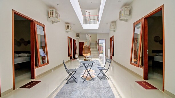 A hotel corridor with a central seating area, doors leading to rooms, a staircase, and a skylight. - Hotel O Madania Guesthouse Syariah (Mataram)