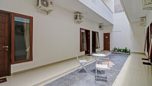 A hotel corridor with a tiled floor, a small round table with chairs, and two air conditioning units mounted on the wall. - Hotel O Madania Guesthouse Syariah (Mataram)