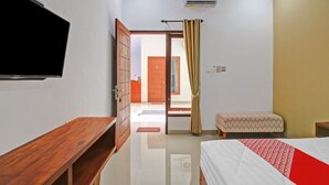 A hotel room with a bed, a wooden bench, a TV, a wardrobe, and an open door leading to another room. - Hotel O Madania Guesthouse Syariah (Mataram)