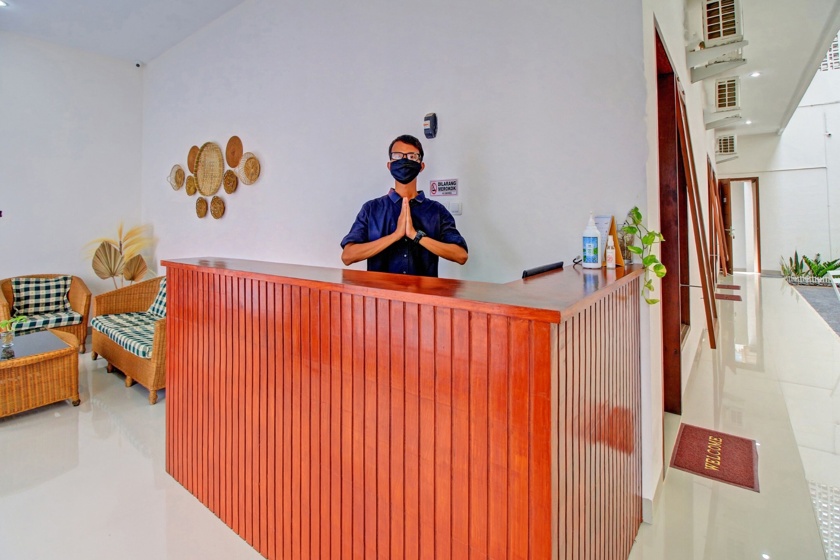 Taulell de recepció d'hotel amb un home darrere, un sofà a quadres i una paret amb plats decoratius.