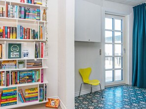 Une pièce avec une bibliothèque remplie de livres, un fauteuil jaune et une fenêtre ornée de rideaux bleus.