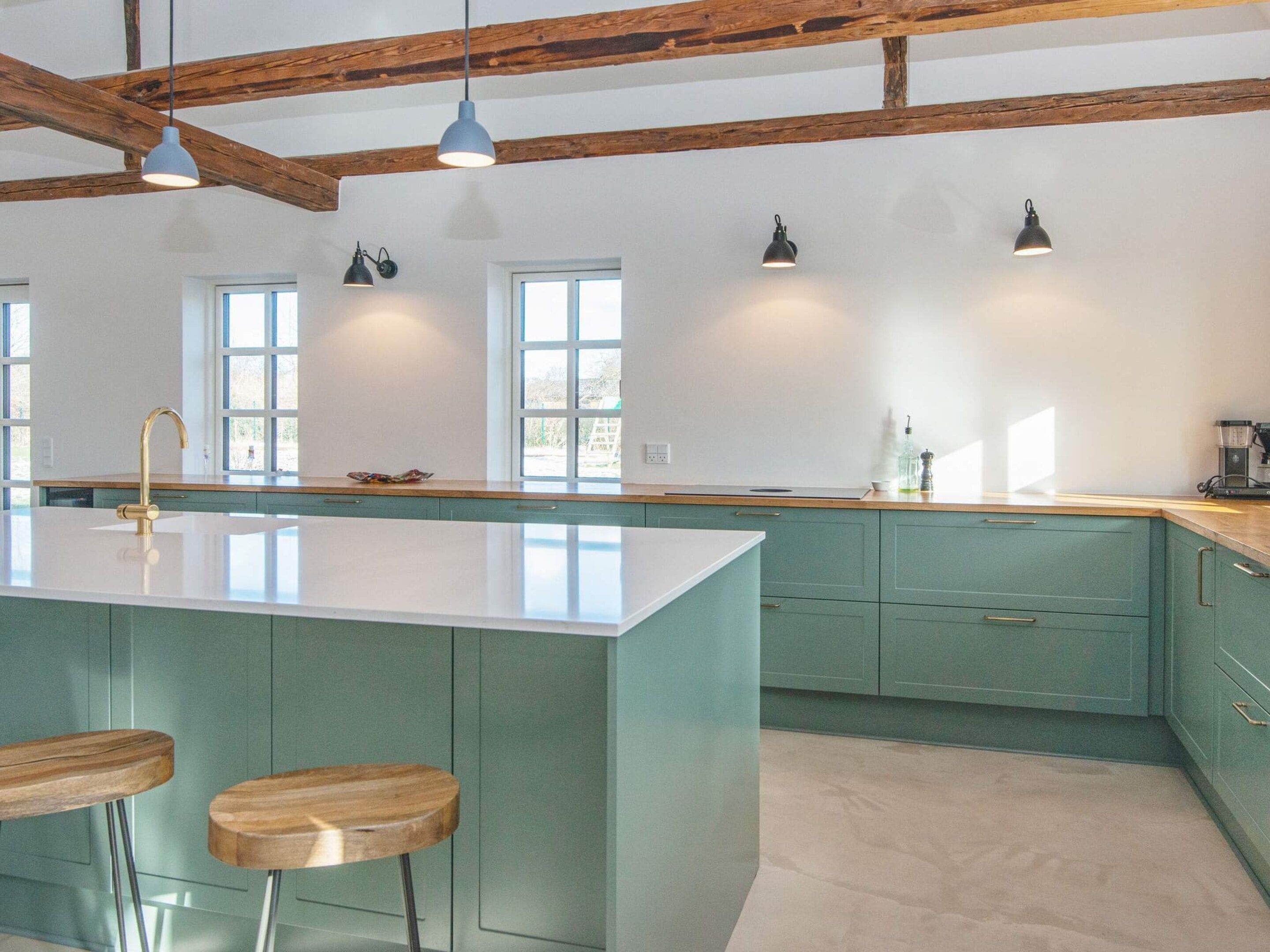 A kitchen with a central island, bar stools, pendant lighting, and wooden beams.