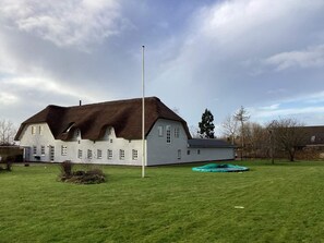 Um edifício grande com telhado de palha, um mastro e um campo gramado.