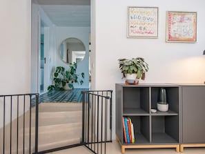 Um corredor com escada, espelho, planta em vaso, estante de livros e duas obras de arte emolduradas na parede.