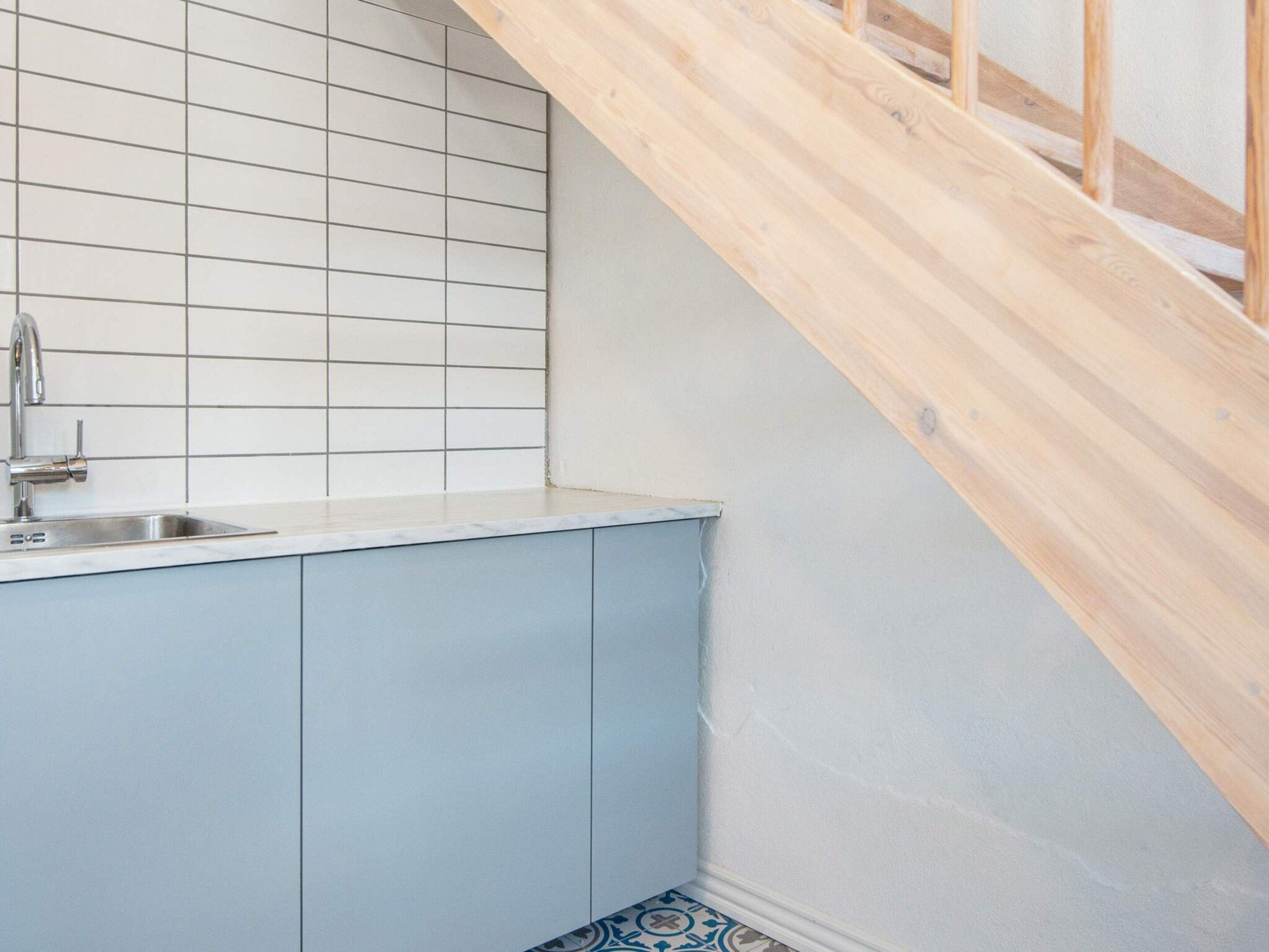 A kitchen with a tiled backsplash, a stainless steel sink, and light blue cabinets.