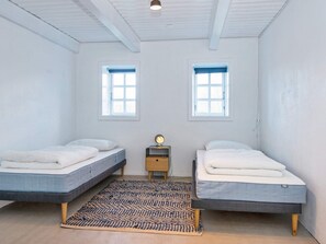 Een kamer met twee bedden, een klein nachtkastje met een lamp, en twee ramen.