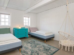 Un dormitorio con dos camas, un aparador azul, una silla colgante y una alfombra estampada.