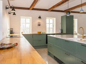 Een keuken met houten balken, groene kastjes, een wit aanrechtblad en hanglampen.