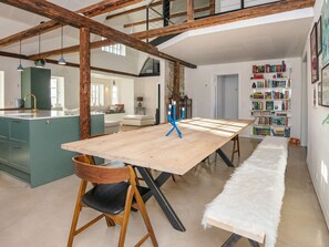 Een ruime woonkamer met een houten eettafel, een boekenkast en een keuken met een spoelbak en kastjes.