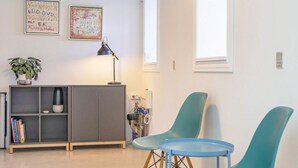 Uma sala de estar moderna com um armário cinza, duas poltronas azul-esverdeadas, uma mesinha, um abajur e uma estante com livros.