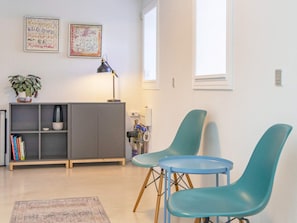 Uma sala de estar moderna com um armário cinza, duas poltronas azul-esverdeadas, uma mesinha, um abajur e uma estante com livros.