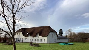A large, white building with a thatched roof, surrounded by a grassy field and a few trees. - 12 Person Holiday Home in Sonder Omme (Sonder Omme)