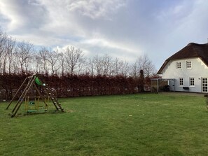 Een gazon met een schommel en een wit huis met rieten dak.