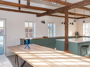 Una cocina moderna con vigas de madera, una isla grande e iluminación colgante.