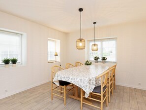 Zona pranzo con tavolo, sedie, lampade a sospensione e piante in vaso.