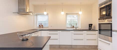 A modern kitchen with a central island, built-in oven, and pendant lighting.