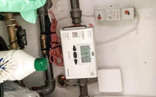 A utility room with exposed pipes, a water meter, and electrical outlets.