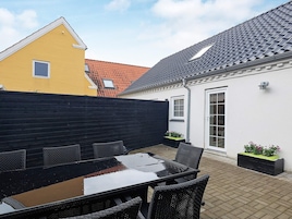 A patio with a table and chairs, a black fence, and a building with a tiled roof.