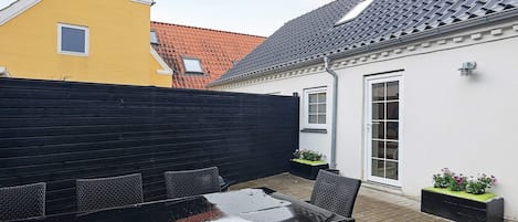 A patio with a table and chairs, a black fence, and a building with a tiled roof.
