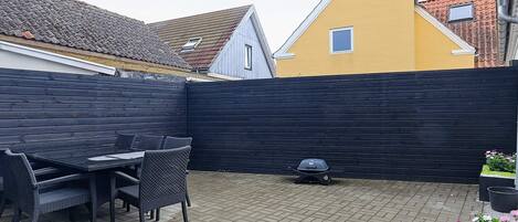 A patio area with a table and chairs, a black fence, and a yellow building in the background.