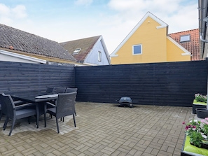 A patio area with a table and chairs, a black fence, and a yellow building in the background.