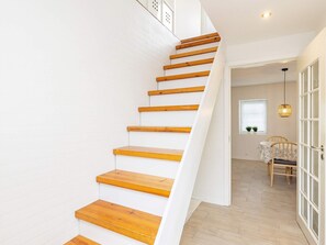 Uma escadaria com degraus de madeira que leva a um quarto com mesa e cadeiras.
